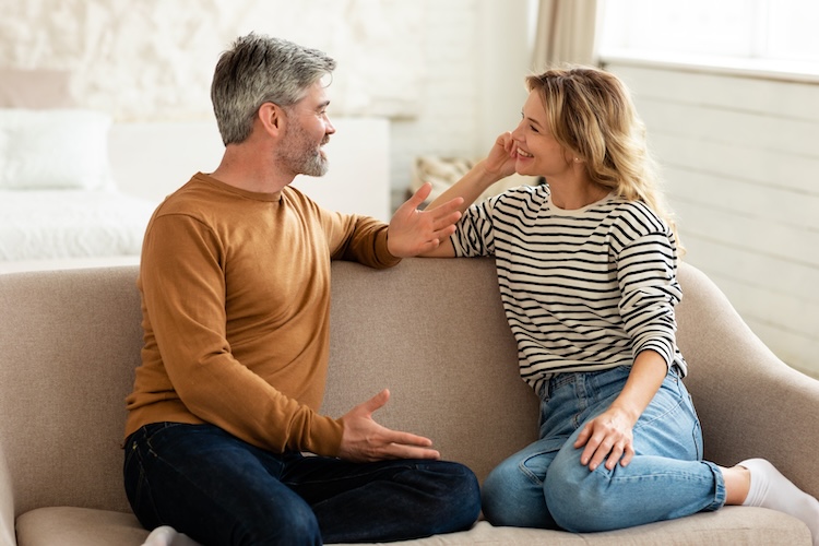 Cheerful Middle Aged Couple Talking And Flirting Enjoying Conversation Spending Time Together Sitting On Sofa At Home. Happy Marriage And Romantic Relationship Concept