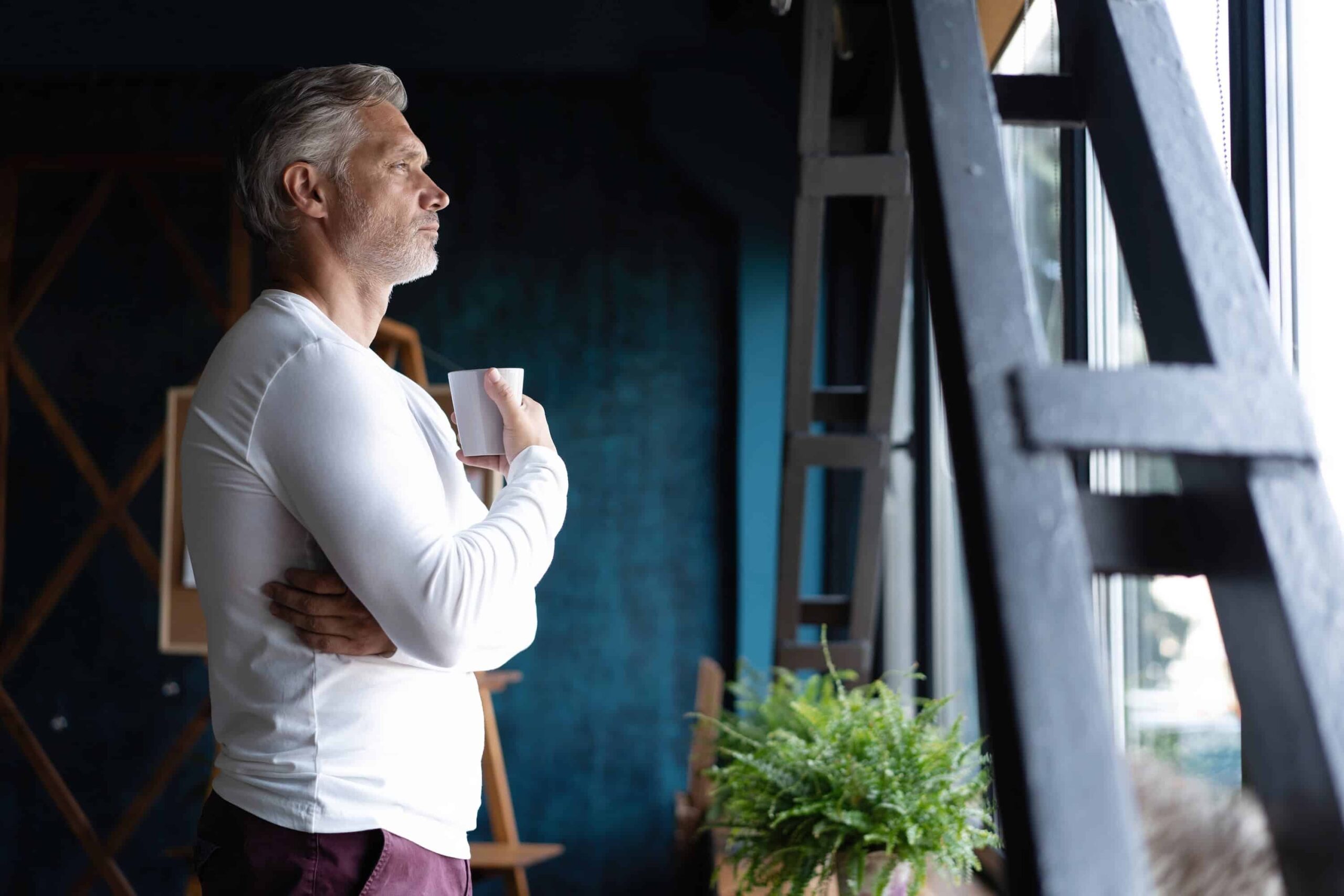 Man standing looking outside window thinking