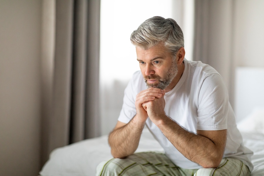 Man sitting on the end of the bed thinking
