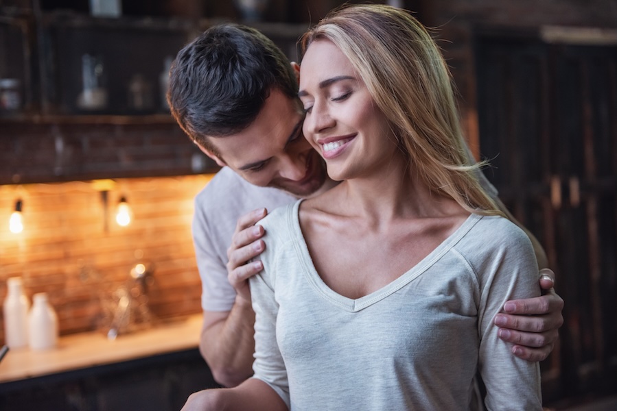 Handsome man is kissing his beautiful girlfriend in shoulder, both are smiling