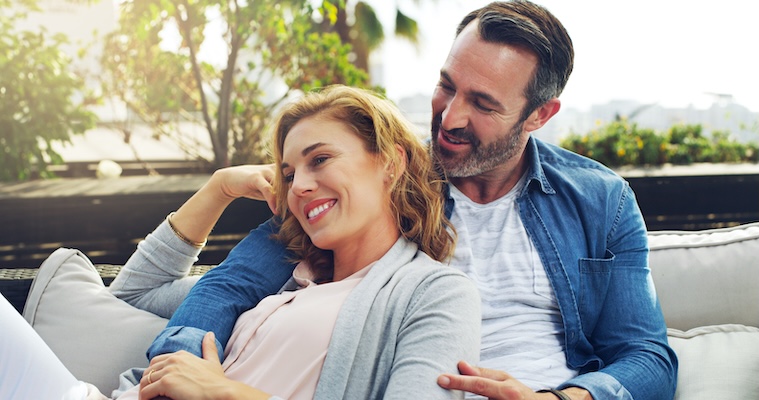 Hug, relax and couple on hotel terrace with smile, love and tropical holiday fun together. Laughing, man and happy woman on outdoor couch with embrace, cozy romance and date on calm travel vacation in australia
