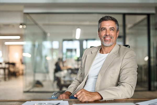 Happy middle aged business man ceo sitting at office desk looking away. Smiling mature confident professional executive manager, 50 years old businessman leader wearing suit, portrait at work.