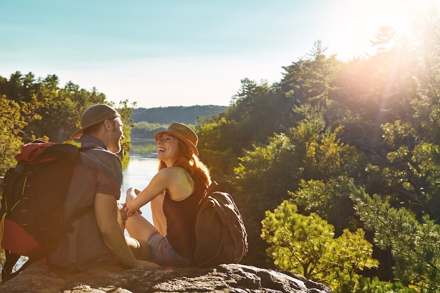 Nature, break and couple with laugh for hiking trip, backpacking adventure and outdoor sightseeing. Happy, space or people with eco tourism for scenic holiday, trekking stop and romantic bonding date